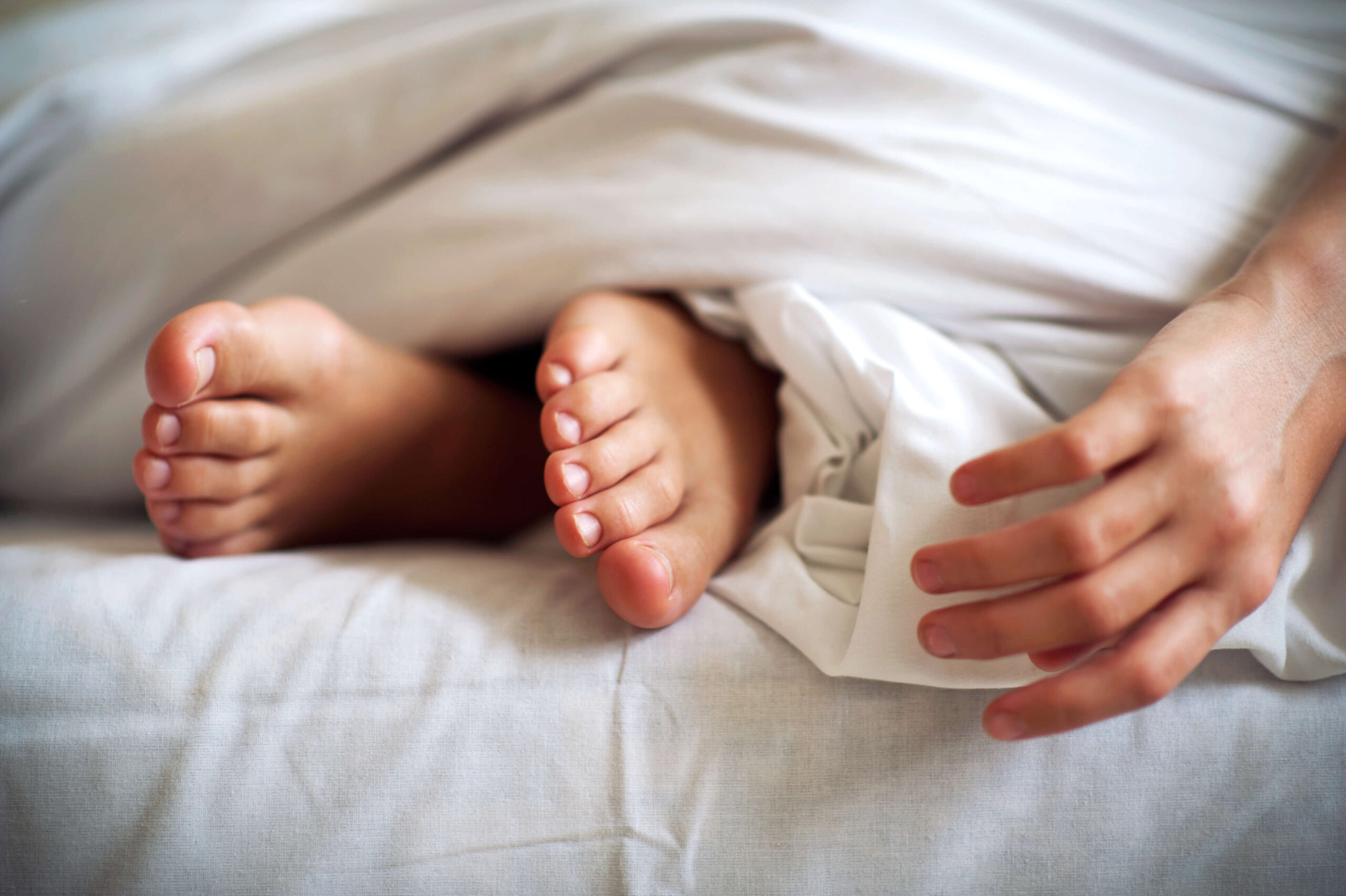 barefoot feet and hand on white bed linen. Indoor