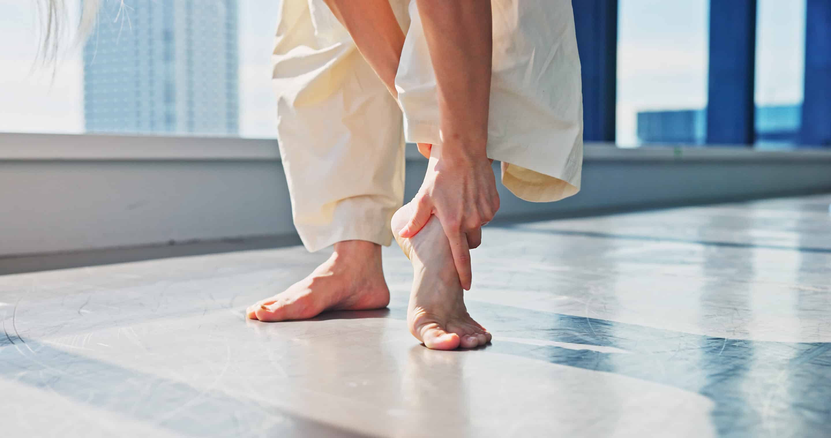 Injury, legs and dancer in studio, hurt and fracture on ankle, joint pain and accident for person. Tension, hands and sore on foot, muscle and inflammation for performer, bone and fitness in Japan