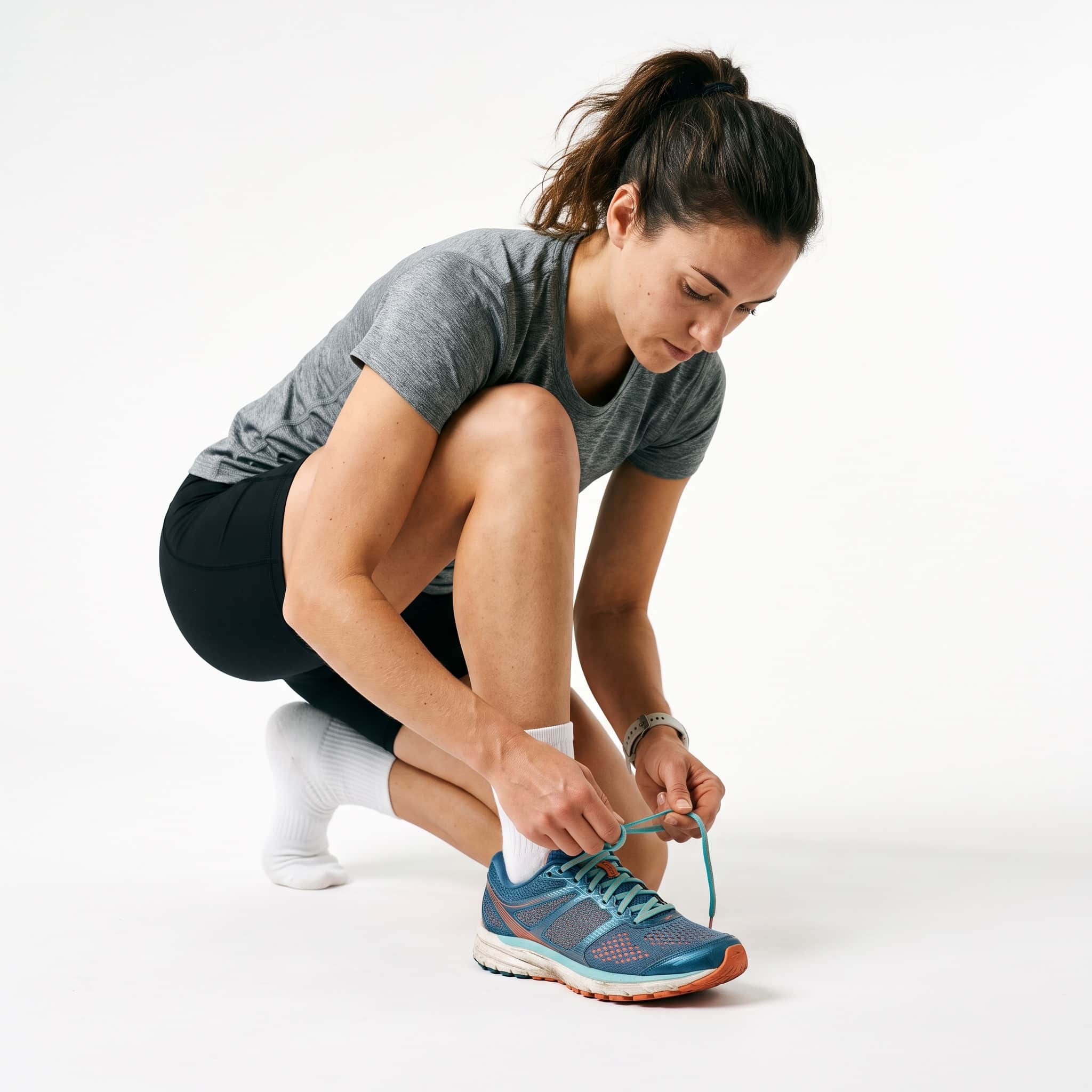 Woman tying shoelaces on athletic shoe while crouching Woman tying shoelaces on athletic shoe while crouching